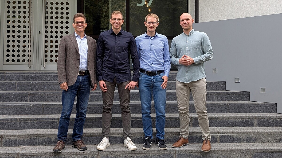 Vier Männer stehen draußen auf einer Treppe vor einer Eingangstür.