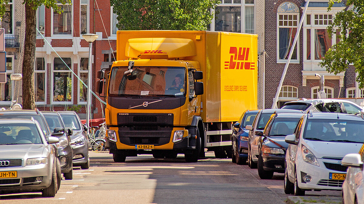 Der Kleinlaster eines Paketdienstleisters biegt in eine enge Straße, in der rechts und links Autos parken.