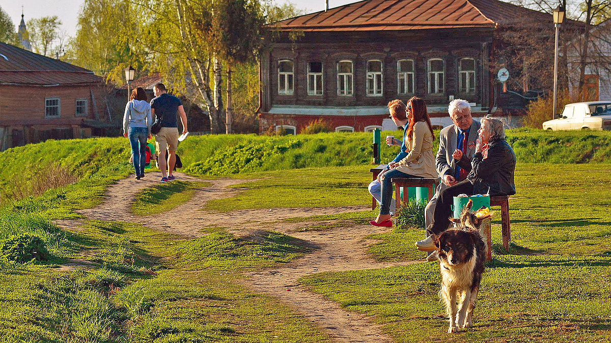 Menschen unterschiedlichen Alters begegnen sich auf einer Wiese mit Bänken.