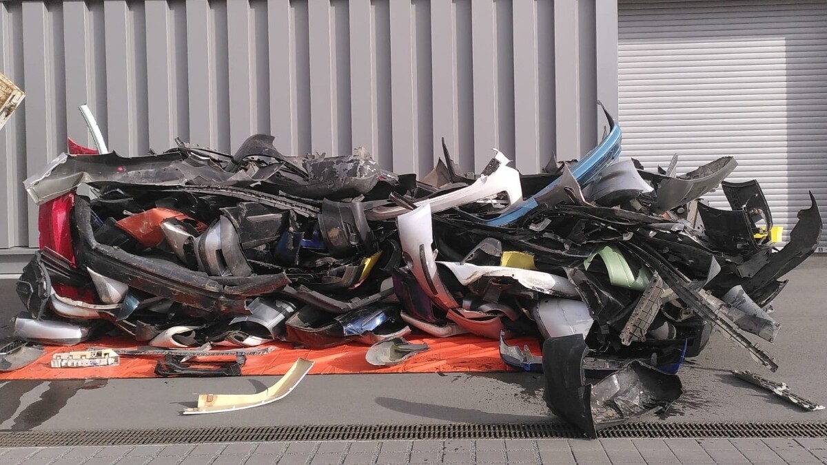 Auf einem Hof liegt ein Haufen schwarzer und bunt lackierter Autostoßstangen.